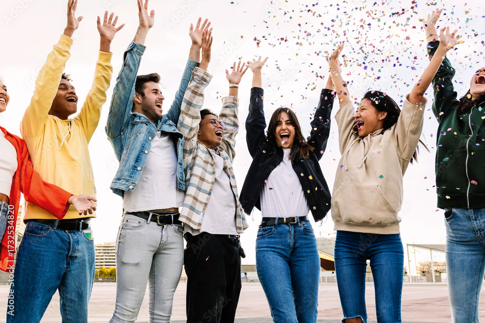 Obraz premium Group of diverse young friends celebrating together enjoying party throwing confetti outdoors - Happiness and celebration concept with millennial multiracial friends laughing and having fun