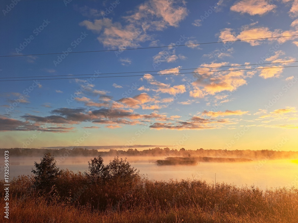 Fototapeta premium Golden sunrise with morning mist, soft blue skies, and a forest in the background. Peaceful and dreamy natural scene perfect for seasonal, landscape, or atmospheric visuals.