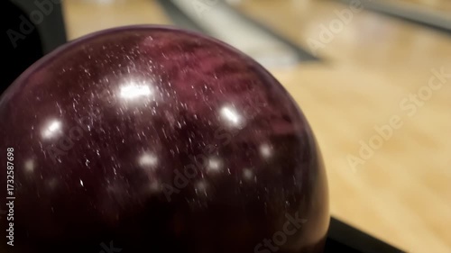 Polished maroon bowling ball with finger hole on a lane