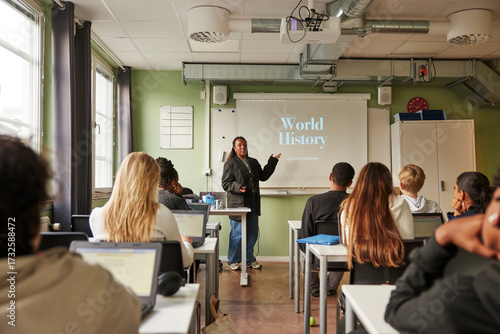 Female professor teaching about world history on projection screen to junior high students in classroom