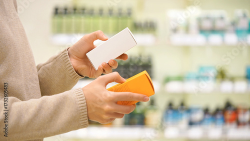 Fotografia Close up of woman holding two cosmetic serums for face or hair in a beauty store, comparing products and reading labels