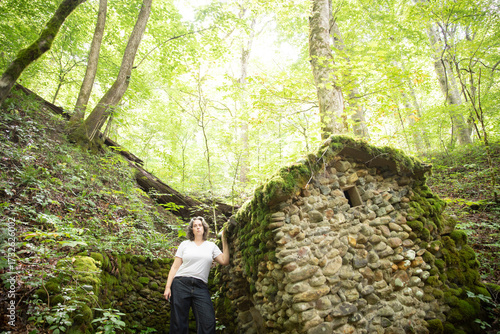 woman by collapsing stone shed in woods