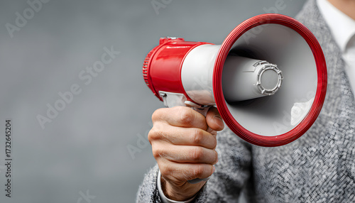 Hand in suit holds red and white megaphone. Isolated on white background. Symbolizes communication, announcement, public speaking, and business or political messaging for crowd.
