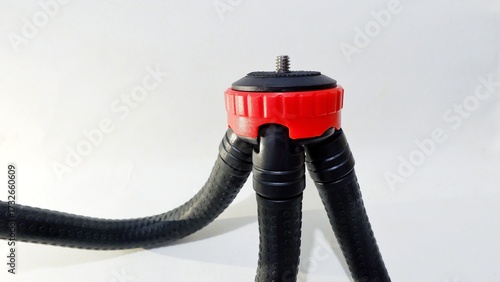 Close-up of a flexible mini tripod with a red and black mount on a white background. Represents photography equipment, camera accessories, and video recording tools concept.