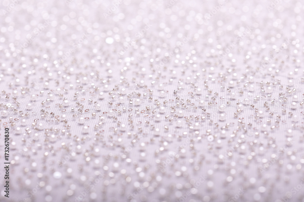 Obraz premium Close-up of elegant, off-white pearl lace fabric with delicate beads and sequins on fine mesh, creating a shimmering texture ideal for fashion, bridal, and luxury design concepts.
