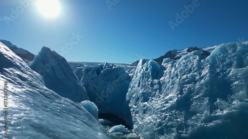 Wallpaper Mural Glacier Ice Formations Under Sunlight - The video shows a glacier with sunlight reflecting off its blue ice formations. The sky is clear and blue, with mountains visible in the distance. Torontodigital.ca