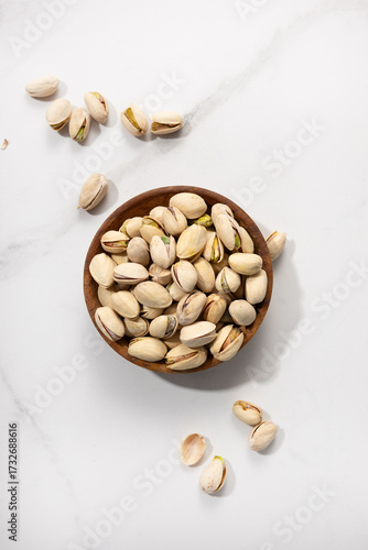 Overhead view of pistachio nuts in bowl on light surface