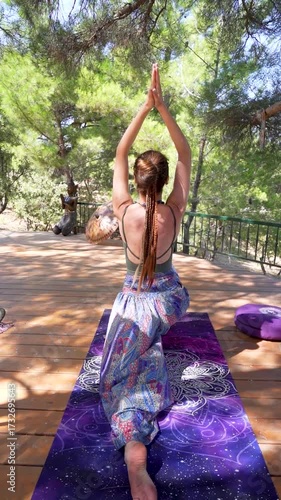 Woman practicing yoga pose outdoors on wooden deck under a tree	
