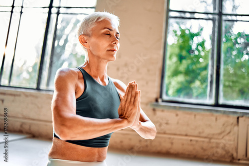 A senior woman holding her hands in a namaste pose while practicing meditation. Yoga practice and spiritual fulfillment.