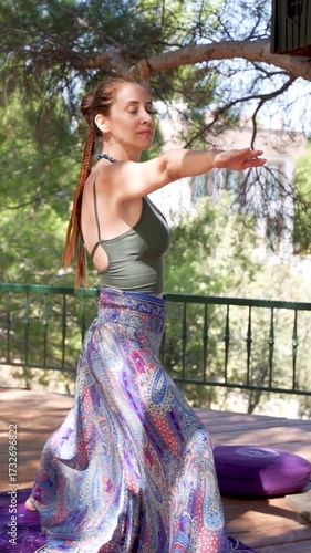 Woman practicing yoga pose outdoors on wooden deck under a tree	