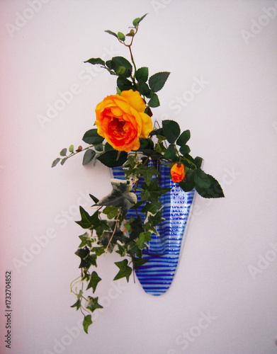 Flower arrangement of yellow roses and ivy in a blue glass pot.