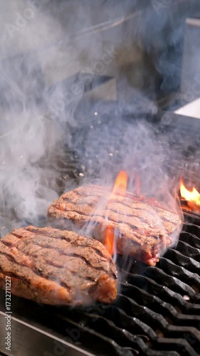 Juicy steaks grilling with flames. Two steaks with grill marks cooking over flames on a smoky grill.