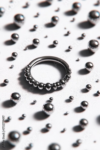 Glossy metal ring with rounded bead texture lies among scattered chrome spheres on a white textured surface