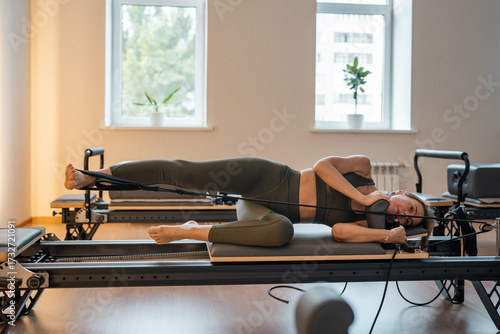 Woman training pilates on the reformer bed. Reformer pilates studio machine for fitness workouts in gym. Fit, healthy and strong authentical body. Fitness concept