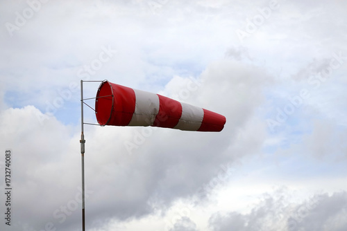 Red and white striped windsock cone shows wind direction and wind speed about 15 knots on aerodrome airfield view close-up