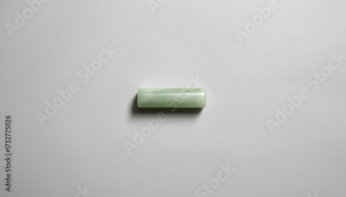 Minimalist flatlay of a single oblong jade stone on a clean white and gray background, highlighting traditional Chinese medicine, skincare tool, and natural mineral beauty.