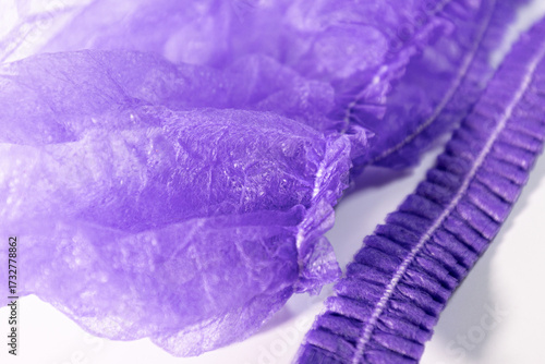 A close-up of a purple disposable hairnet along with a crinkled elastic hair band on a white background with soft lighting and visible texture.