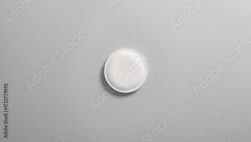 overhead flatlay of a single, pristine white cotton pad or make-up removal disc centered on a clean light gray background, ideal for beauty, skincare, and medical themes.