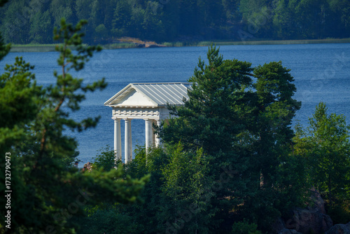 White neoclassical pavilion by the lake surrounded by forest