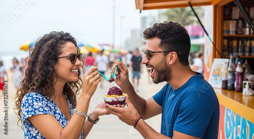 Joyful couple shares a delicious acai bowl on a vibrant beach boardwalk, capturing a perfect summer moment of connection and refreshing treat.