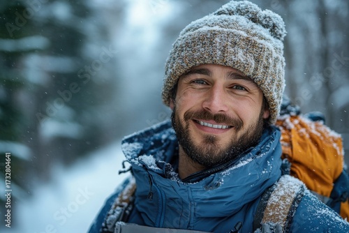 A man in a blue jacket and hat smiles while walking through the snow.