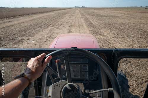 Detalle mano en volante de tractor en campo agrícola arado