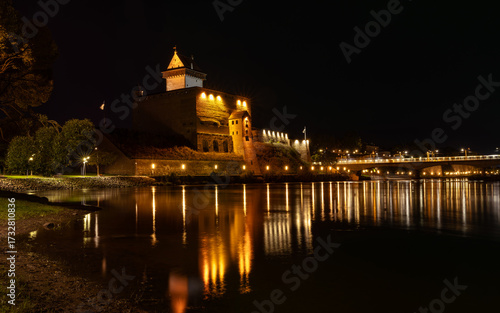 Narva Castle in Estonia illuminated at twilight with reflections in the Narva River, facing Ivangorod Fortress in Russia.