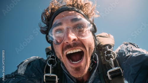 Excited skydiver with goggles and parachute gear screaming with joy during freefall against bright blue sky background