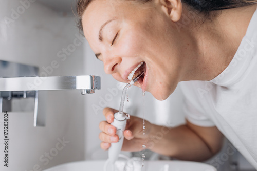 Fotografi A young woman uses a portable water flosser for oral care in the bathroom