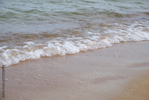 Fototapeta Naklejka Na Ścianę i Meble -  Wave splashing on sandy beach, clear Baltic sea water, foam, natural coastline. Bright outdoor scene, travel, summer, relaxation, peaceful nature