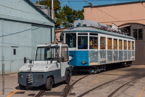 Old tram of opicina tram system is being renovated on the siding tracks of Opicina train station, visible orange curtains and sanded down body of a tram, tractor in the front