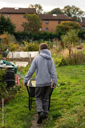 Young Boy Walking Through Allotment with Wheelbarrow on Autumn Day