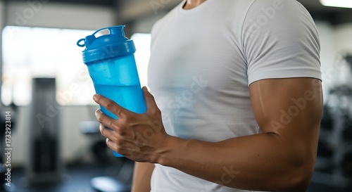 Man holding a blue water bottle inside a fitness gym with copy space