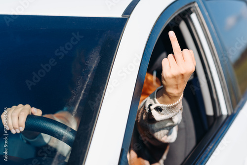 young woman driver gives middle finger to another driver, making obscene gesture, rudeness on roads, road rage concept