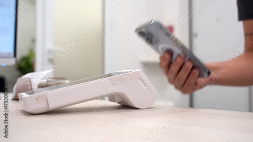 Pay by phone on electronic payment machine or card reader. E-money at cashless wallet. Female hand with pos-terminal and cellphone closeup. Client pays for the procedure in modern beauty clinic.