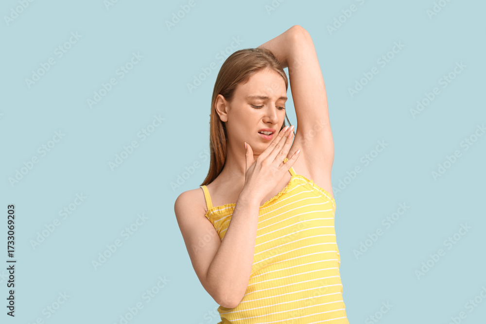 Fototapeta premium Young woman feeling smell of sweat on blue background. Concept of using deodorant
