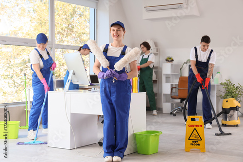Female janitor with pp-dusters and her team cleaning in office