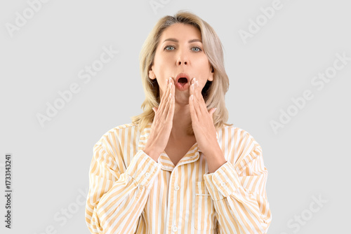 Tableau sur toile Beautiful woman in pajamas doing face building exercise on light background