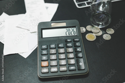 Financial Strain. Calculator displaying the year 2026. glass jar spilling coins. Stress and strain of financial in the coming years. inflation, the rising cost of living, economic forecast.
