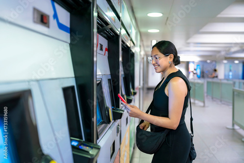 Canvas Print Young smiling Latina woman at a London Underground station in England pays for metro access using a digital card on her smartphone