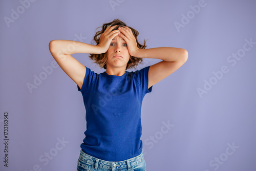 Disappointed young female showing loss with head in hands and sad vibe for failed plans on vibrant blue studio background with upset energy