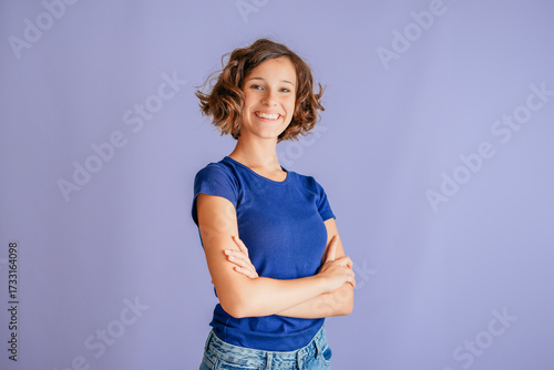 Confident young woman showing powerful gesture with proud smile for motivation on vibrant blue studio background with positive energy