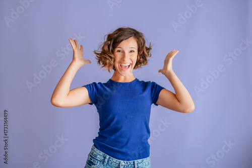 Joyful young girl laughing with open mouth in happy surprise reacting to good news on vibrant blue studio background with genuine joy