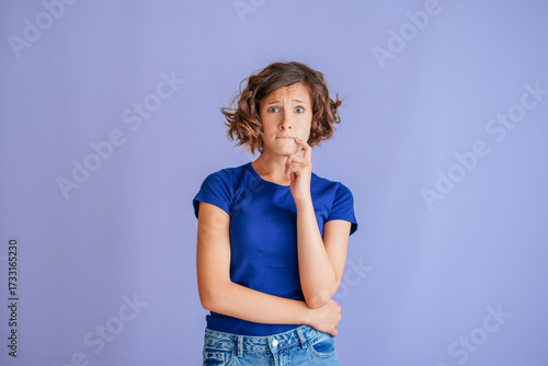 Anxious teenage girl with tense expression feeling nervous on vibrant blue studio background with tense mood