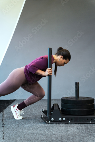 Latin american woman engaging in intense sled push exercise at the gym, building strength and improving fitness
