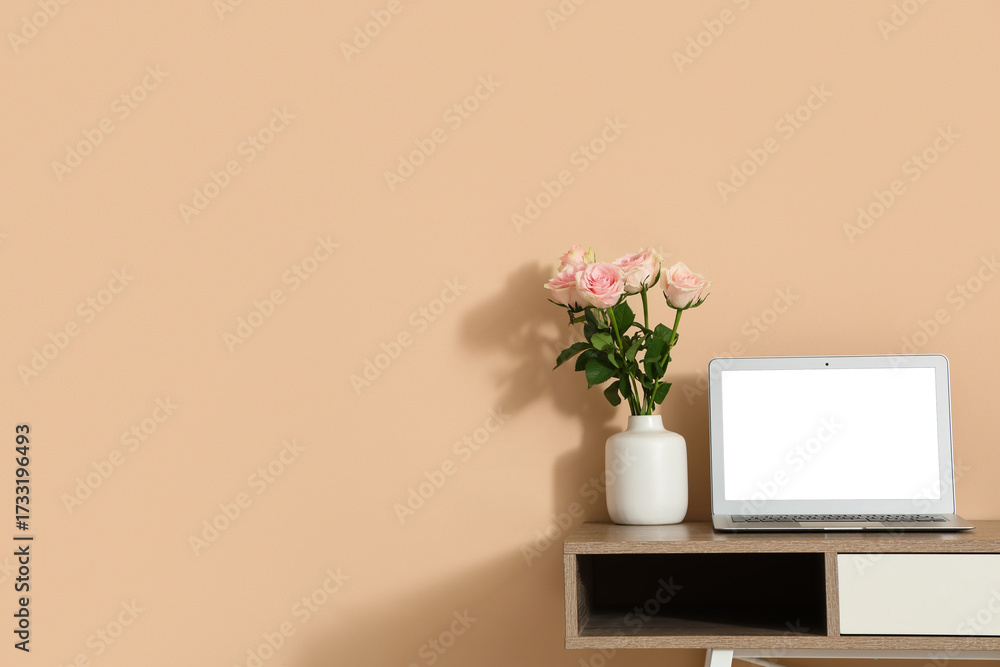 Fototapeta premium Stylish workspace with modern laptop and beautiful flowers near beige wall
