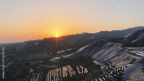 aerial video of the solar power plant at sunset over mountainous landscape
