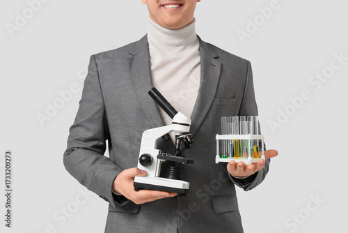 Young male teacher with microscope and chemical flasks on grey background, cl...