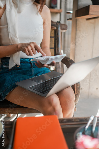 Papier peint A woman in casual attire uses a calculator and laptop, focusing on financial planning and budgeting in a relaxed environment