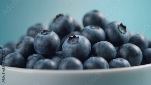 Fresh blueberries tumbling into a white bowl with a vibrant blue background in a dynamic video